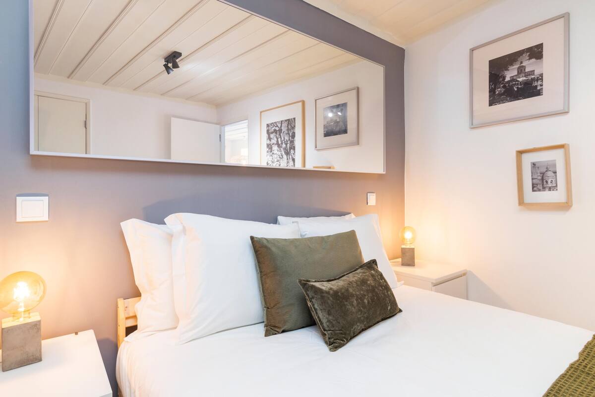 A neatly made bed with white and green pillows, a bedside lamp, and framed pictures on the wall.