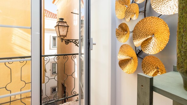 Un balcón con barandilla de hierro forjado, una lámpara fijada a la pared y elementos dorados decorativos circulares.
