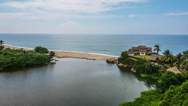 Vista costera con playa, un pequeño cuerpo de agua y un edificio con techos de paja.