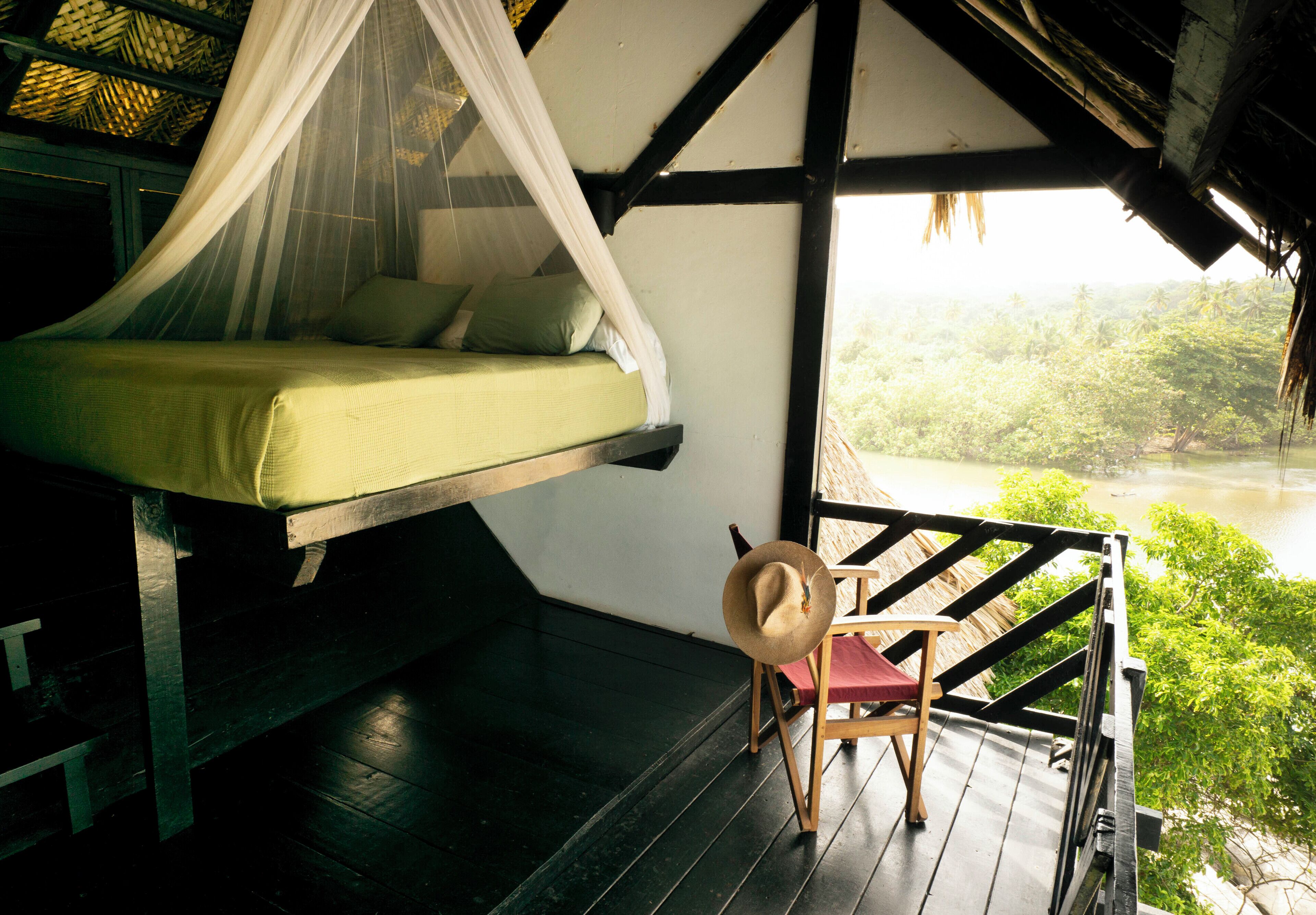 Una cama con dosel, una silla y vistas a un río.