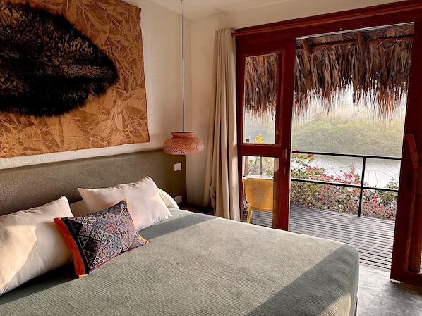 A bedroom with a large bed, a wooden headboard, a hanging light fixture, and a view of a water body outside. - Cabaña Barlovento (Santa Marta)