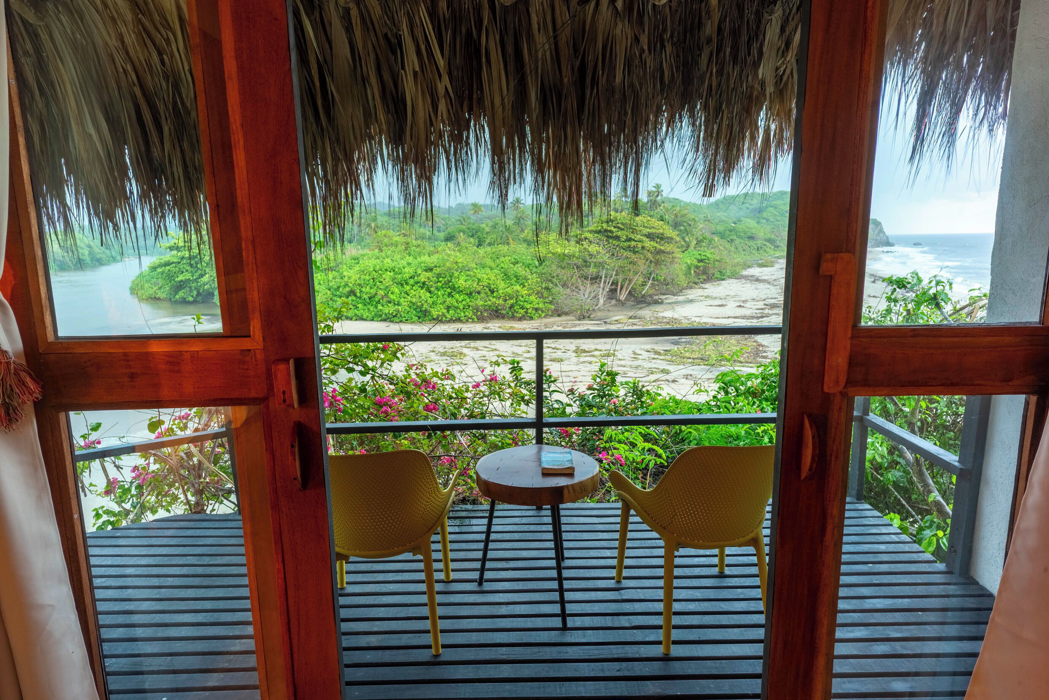 A wooden deck with a thatched roof, two yellow chairs, and a small table.