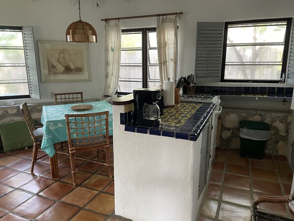 A kitchen with a tiled backsplash, a coffee maker, and a dining area with a table and chairs. - Little House Cottage (Rokers)