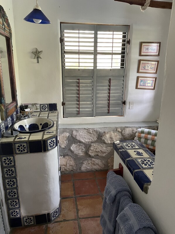 Un baño con pared de piedra, un lavabo con azulejos decorativos, una ventana con contraventanas y un perchero.