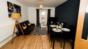Un salon moderne avec un canapé noir, une table à manger dressée pour quatre personnes et un tapis à motifs chevrons noir et blanc.