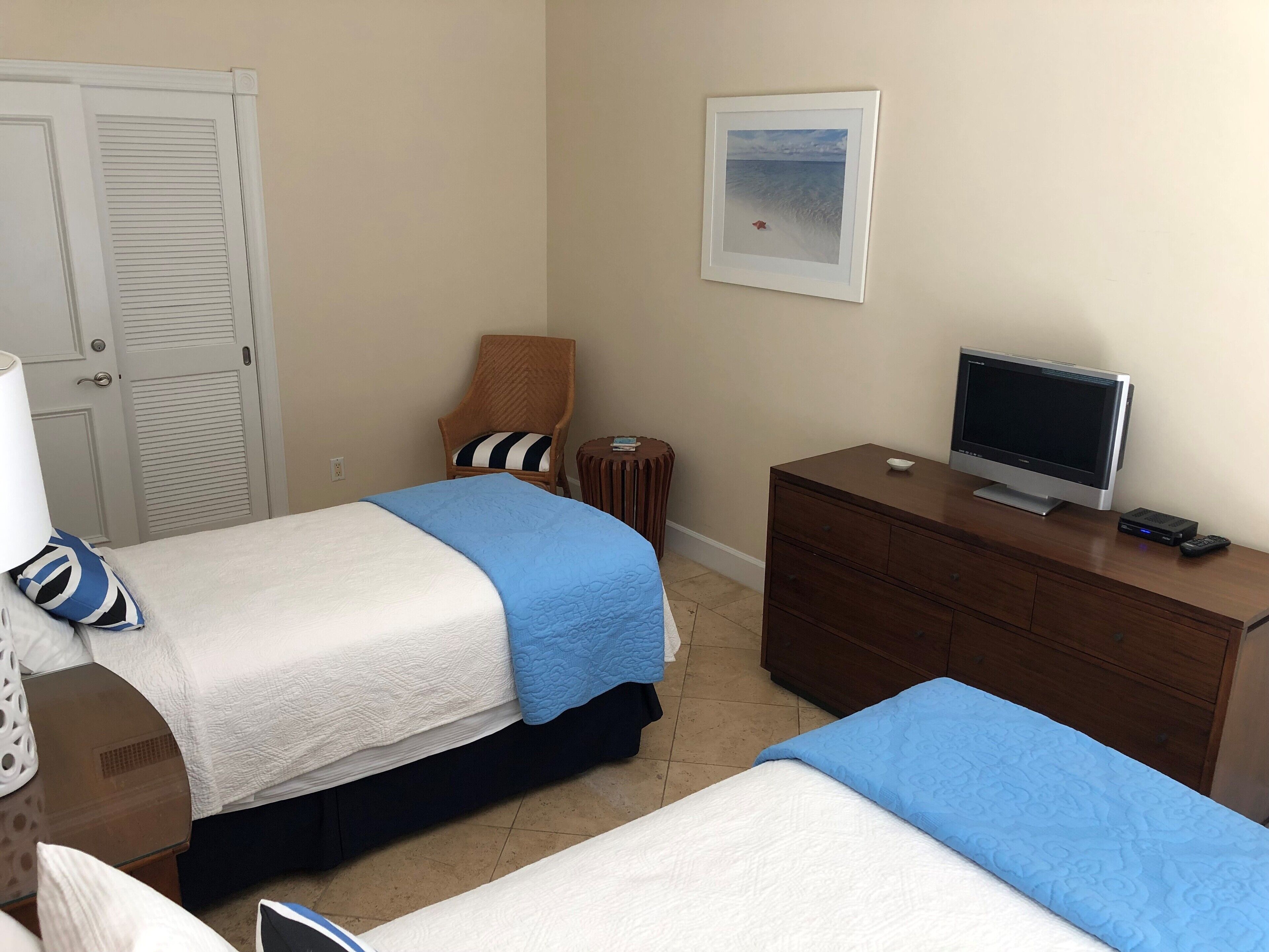 A hotel room with two beds, a television on a dresser, a chair, and a framed picture on the wall.