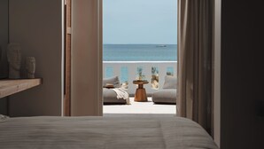 A bedroom with a bed, a wooden nightstand, and a view of the sea through an open door. - Almiriki Naxos Beachside Living (Naxos)