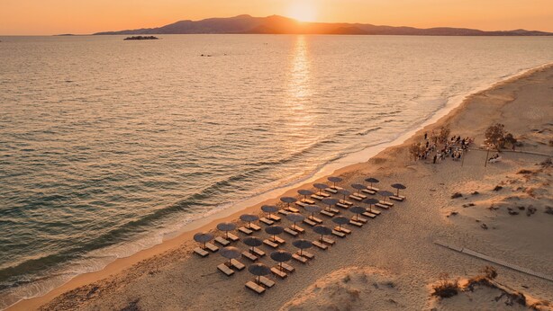 A beach with sun loungers and umbrellas, a clear sky, and a sunset over the water. - Almiriki Naxos Beachside Living (Naxos)