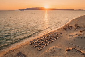A beach with sun loungers and umbrellas, a clear sky, and a sunset over the water. - Almiriki Naxos Beachside Living (Naxos)