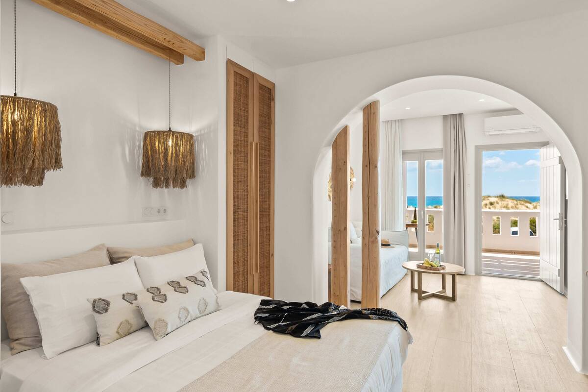 A bedroom with a bed, bedside lamps, a view of the balcony, and a wooden ceiling.