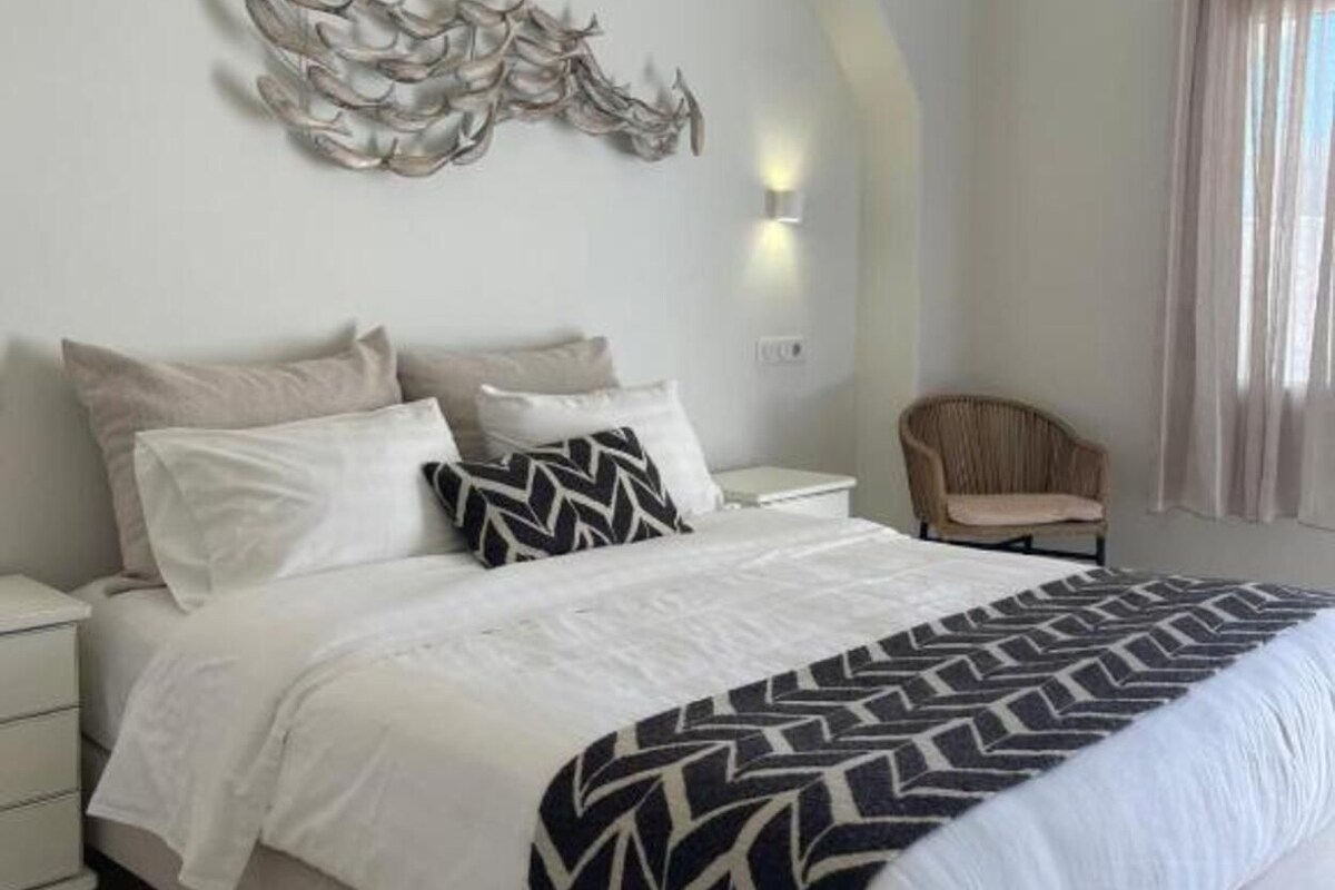 Un dormitorio con una cama, mesitas de noche, una silla y un adorno en la pared.