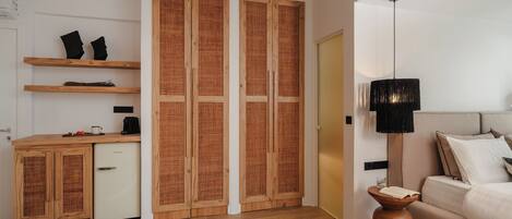 Un dormitorio moderno con suelo de madera, una cama con ropa de cama blanca, una mesita de noche con lámpara y un armario con panel trasero tejido.