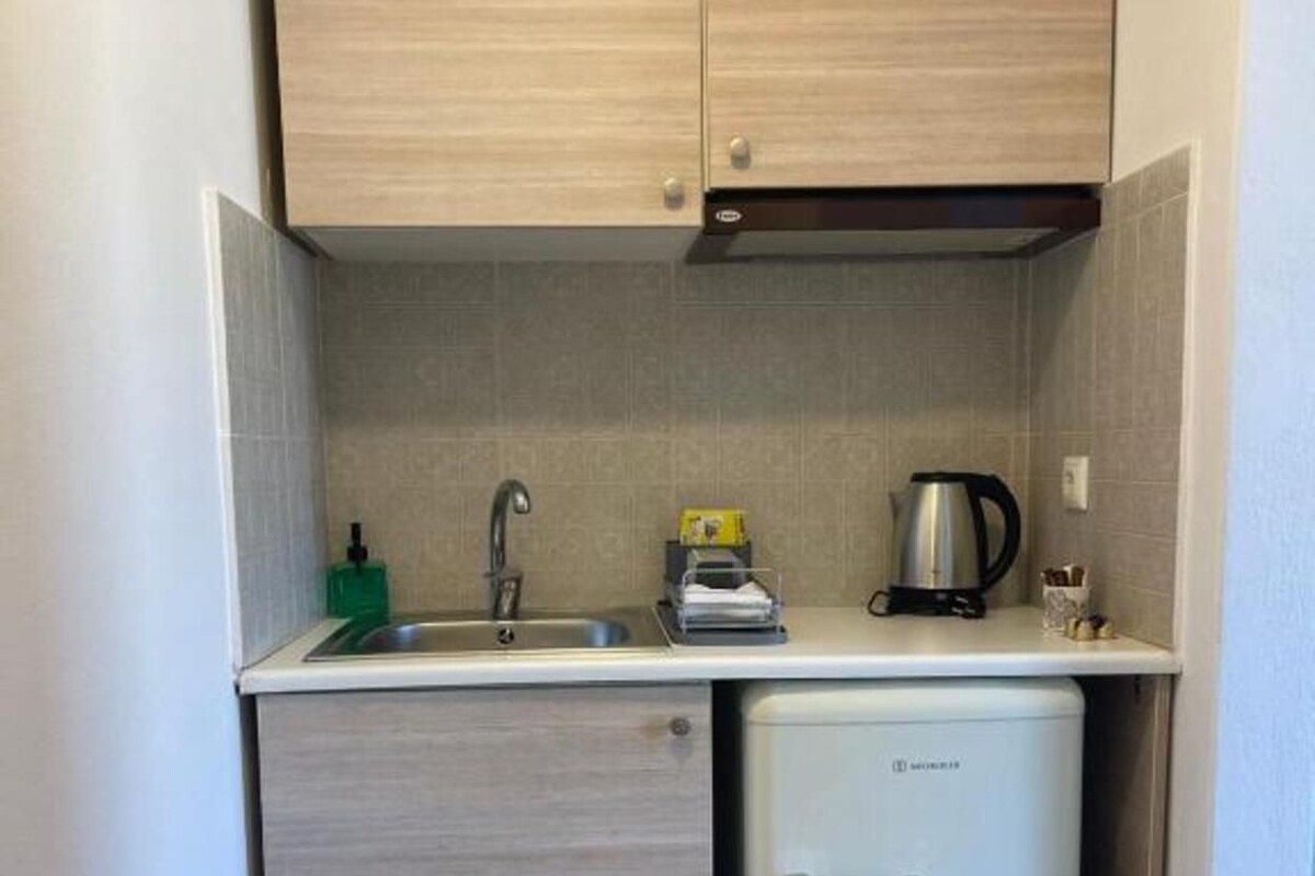 Una kitchenette compacta con un lavamanos, un refrigerador pequeño y una cafetera.