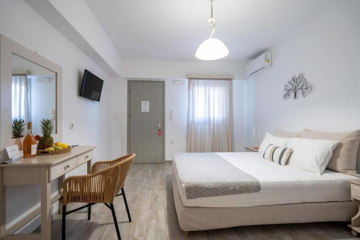 A hotel room with a bed, a desk with a chair, a television, and a window with curtains.