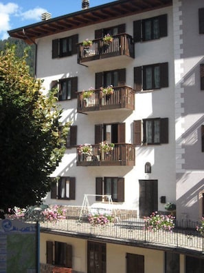 A multi-story building with balconies adorned with flowers, a visible staircase, and a clear sky.