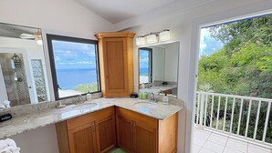 Une salle de bain avec une grande fenêtre, un tapis vert, des meubles en bois et une balustrade de balcon blanche.