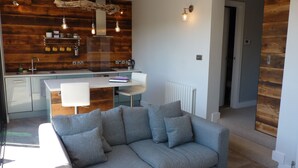 Eine moderne Küche mit Holzakzenten, ein Essbereich mit weißem Tisch und Stühlen sowie ein graues Sofa in einem Wohnbereich.