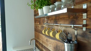 Eine Küche mit Holzrückwand, Spüle, einer Pflanze und Küchenutensilien, die an einem Gestell hängen.