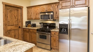 A kitchen with wooden cabinets, stainless steel appliances, granite countertops, and a built-in microwave. - Comfortable Condo - Convenient Upper Village Location (Whitefish)