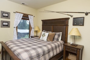 A bedroom with a large bed, two bedside tables, a window with curtains, and wall-mounted lamps.