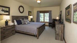 A bedroom with a large bed, bedside tables, a desk, and a chair. There is a window with curtains, a wall-mounted light, and framed pictures. - Hotel Style Room Near Slopes (Whitefish)