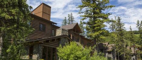 A log cabin with a stone chimney, surrounded by dense forest and a clear sky.