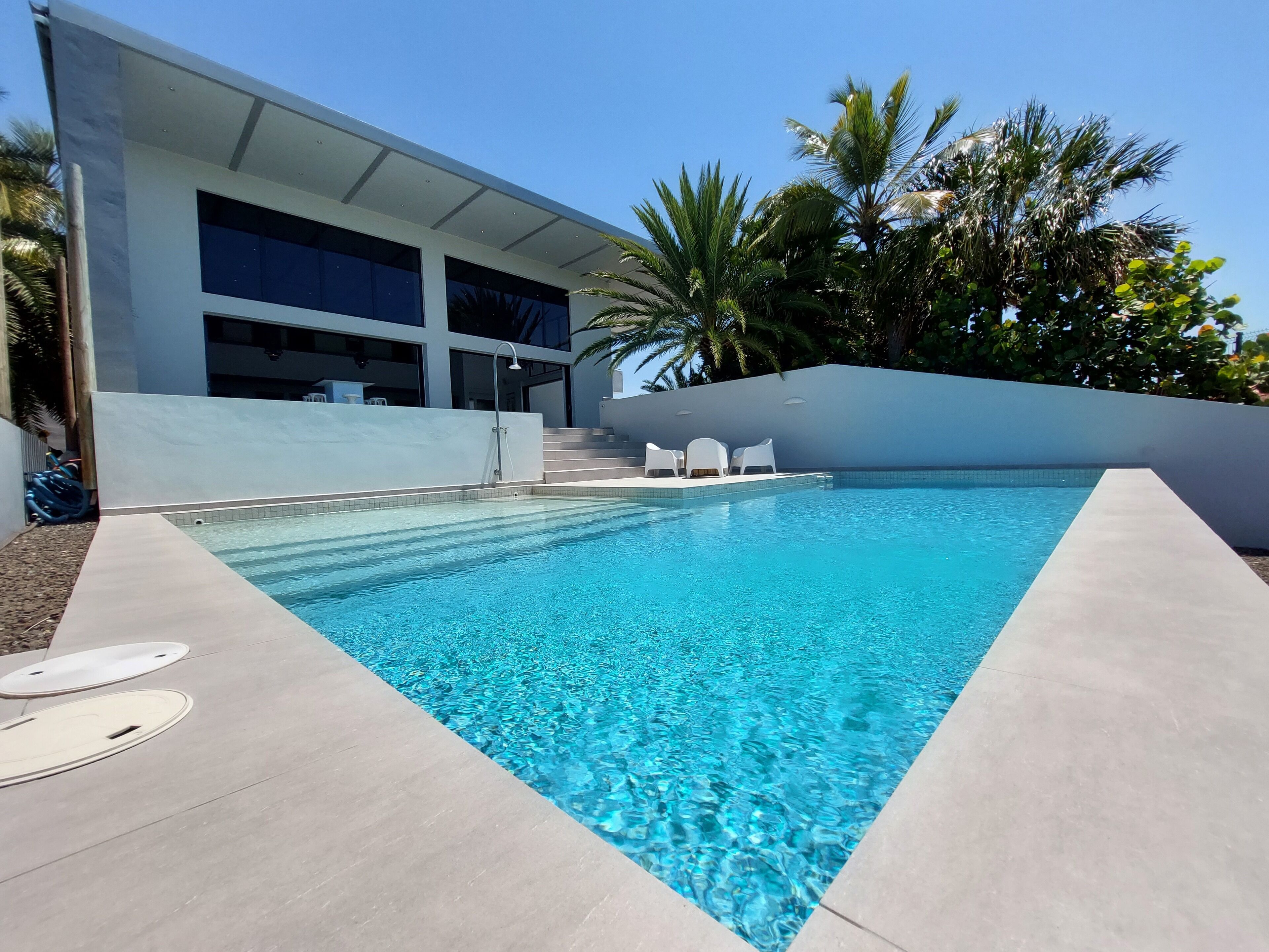 A modern pool area with clear blue water, white lounge chairs, and a building with large windows and a covered patio.