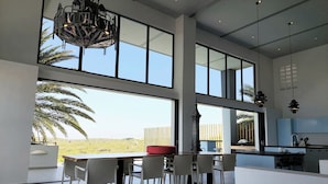 Una cocina amplia con ventanas grandes, un comedor con sillas blancas y vistas a un paisaje verde.