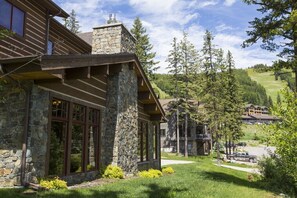 Un bâtiment en pierre et en bois, doté de grandes fenêtres, entouré d’une zone herbeuse et d’arbres.