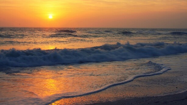Ein Sonnenuntergang über dem Meer, wobei Wellen auf das Ufer zulaufen.
