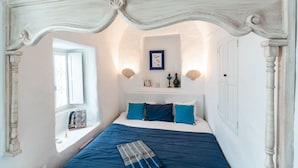 Une chambre à coucher avec un lit à baldaquin, une fenêtre donnant sur un beau paysage et une étagère ornée d’objets décoratifs.