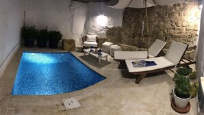 Une piscine avec un mur en pierre et des chaises longues.