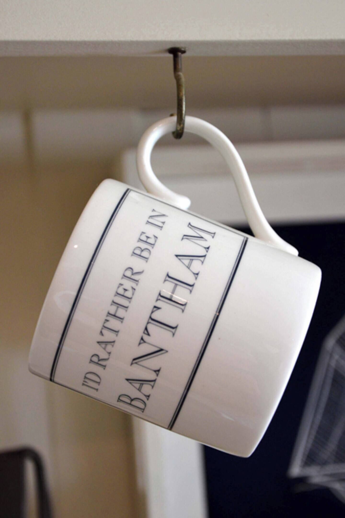 Een witte mok met de tekst 'I'd rather be in Bath than...' hangt aan een haak.