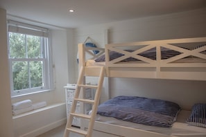 Une chambre avec un lit superposé, une échelle, une fenêtre et un mur blanc.
