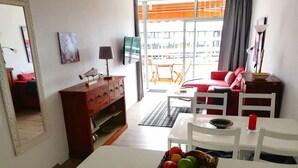 Ein Wohnzimmer mit Esstisch, einem roten Sofa, einer Holzkommode und einem Fernseher.