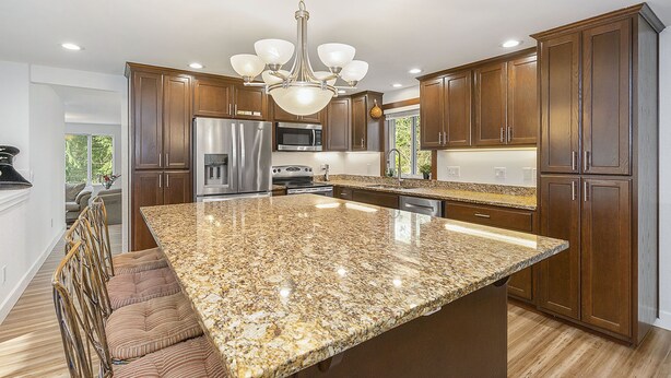 Una cocina con encimeras de granito, electrodomésticos de acero inoxidable, armarios de madera y una isla central.