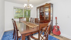 Un comedor con una mesa de madera, sillas, una araña, una vitrina de vidrio y una guitarra.
