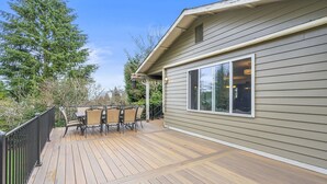Una terraza con mobiliario exterior y una casa con revestimiento y un amplio ventanal.