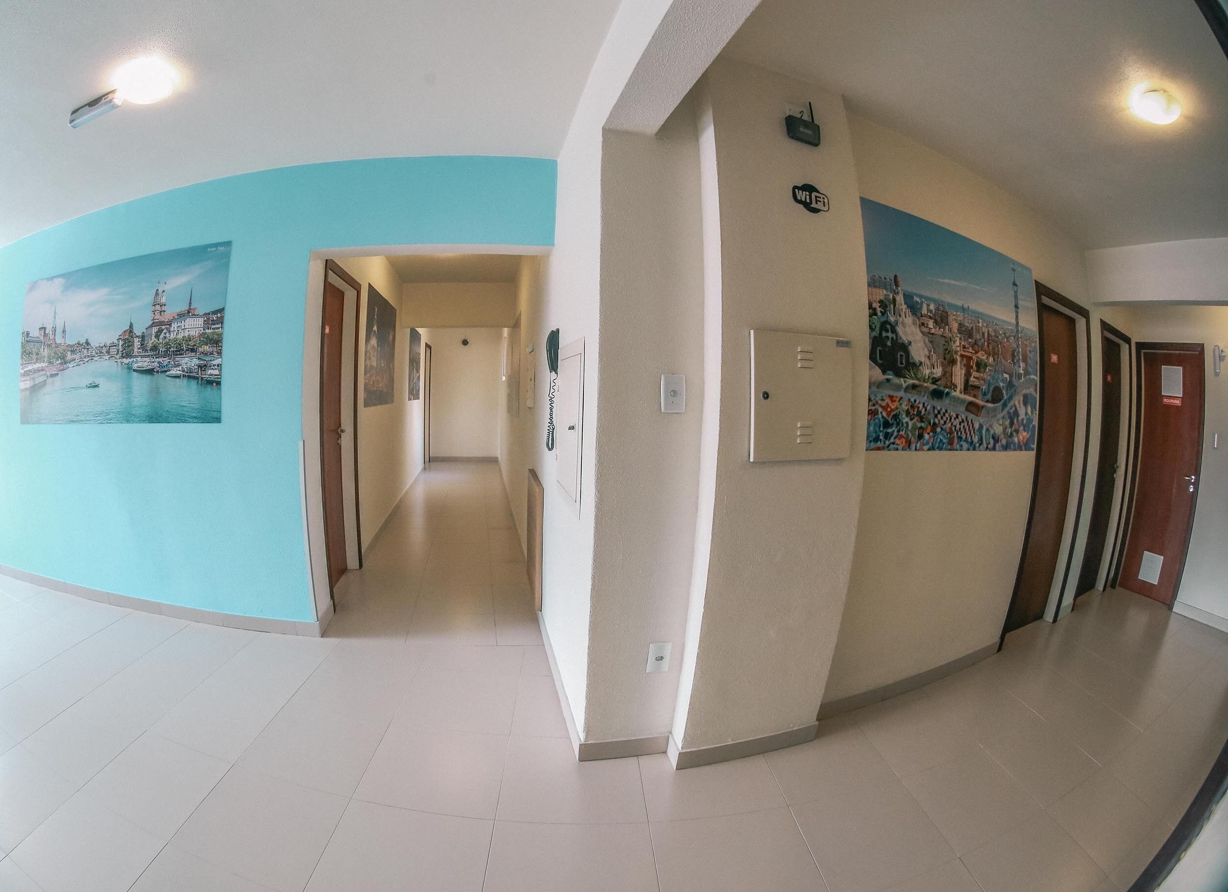 Un couloir d’hôtel avec un mur incurvé orné d’une fresque représentant un paysage urbain, un interrupteur et un panneau indiquant la présence d’une connexion Wi-Fi.