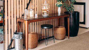 A wooden partition with vertical slats, a table with glass jars, a potted plant, and wicker baskets. - Rede Andrade Criciúma (Criciuma)