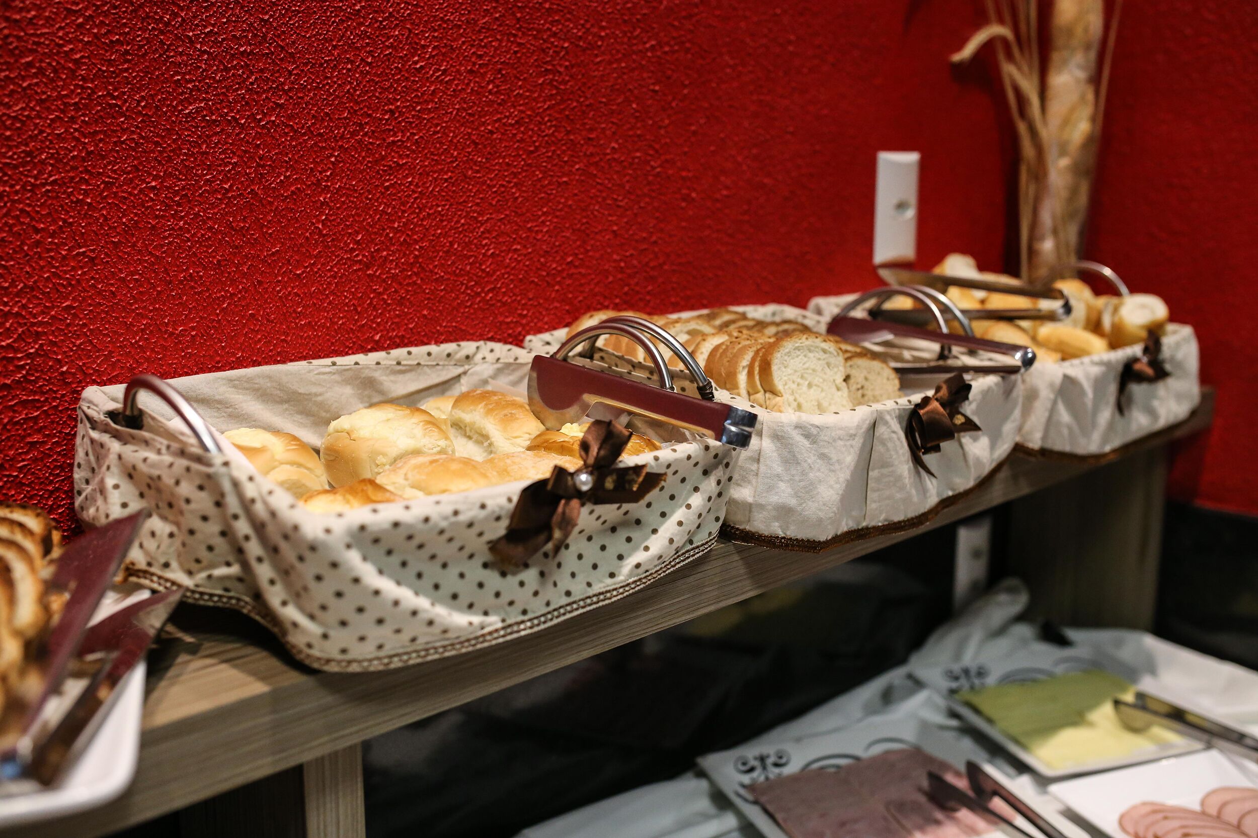 Mesa con panes y pasteles en un buffet, con una pared roja de fondo.