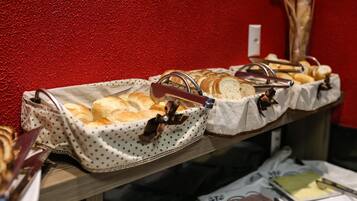 Mesa con panes y pasteles en un buffet, con una pared roja de fondo.