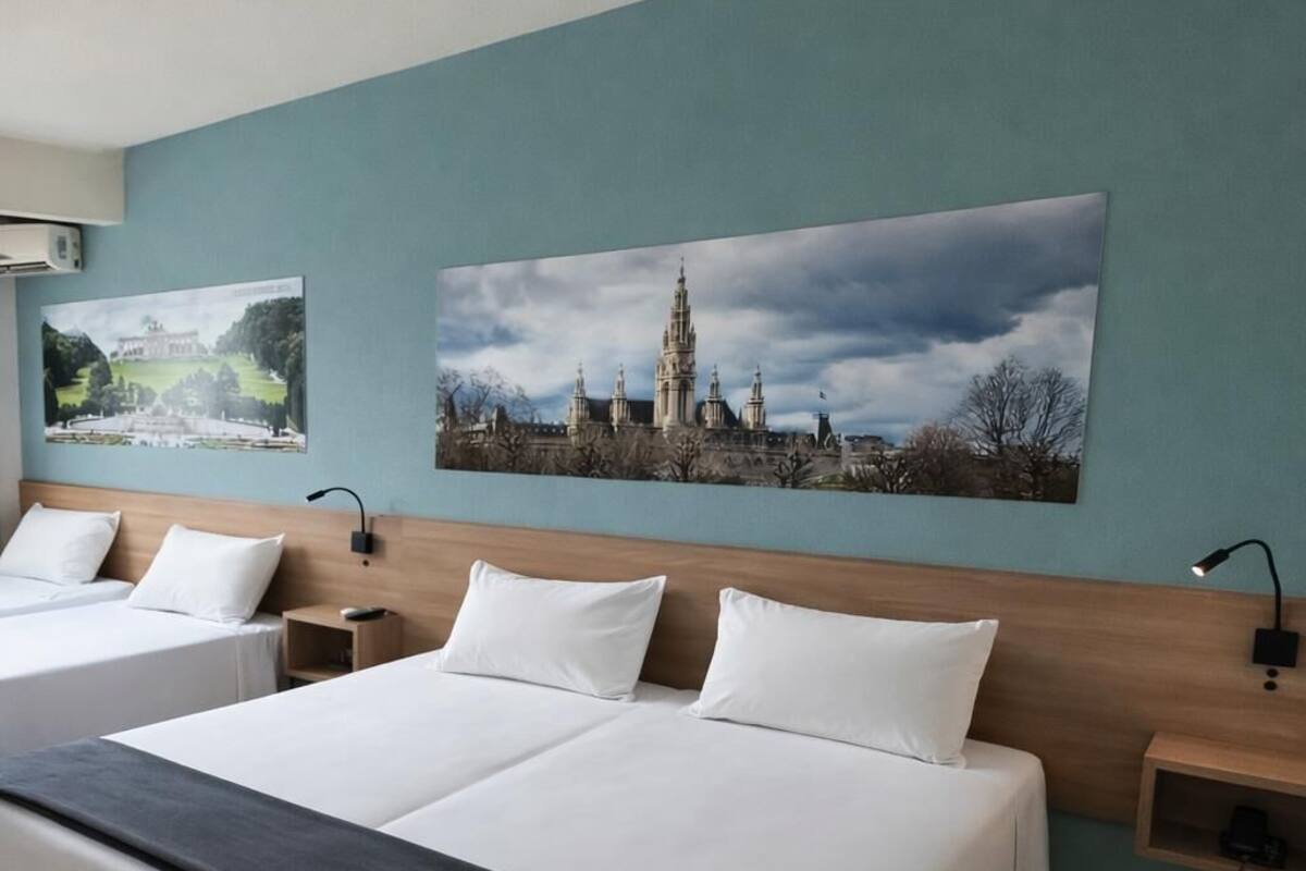 A hotel room with two beds, a large window, and artwork on the wall.