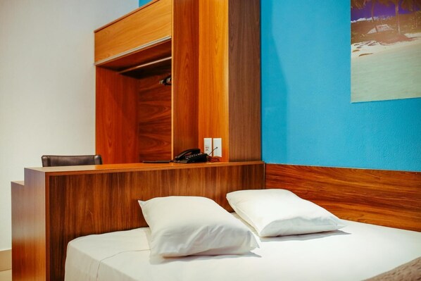 Una habitación de hotel con un escritorio de madera, un teléfono y una cama con almohadas blancas.