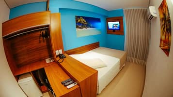 Quarto de hotel com escrivaninha de madeira, cama, televisão e mini-frigorífico.