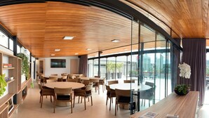 A spacious indoor area with round tables and chairs, wooden ceiling, large windows, and a reception desk. - Rede Andrade Criciúma (Criciuma)
