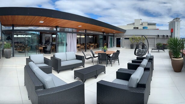 An outdoor patio area with wicker furniture, a wooden canopy, and a glass wall overlooking the street. - Rede Andrade Criciúma (Criciuma)