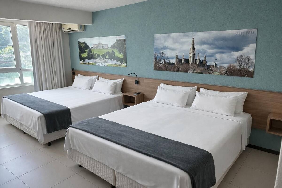 A hotel room with two beds, a large window with curtains, and two wall-mounted paintings.