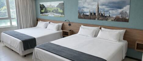 A hotel room with two beds, a large window with curtains, and two wall-mounted paintings.