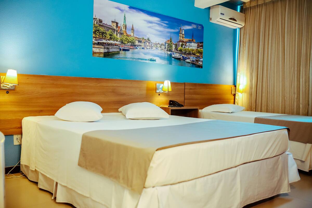 A hotel room with two beds, a wooden headboard, a cityscape mural, and an air conditioning unit.